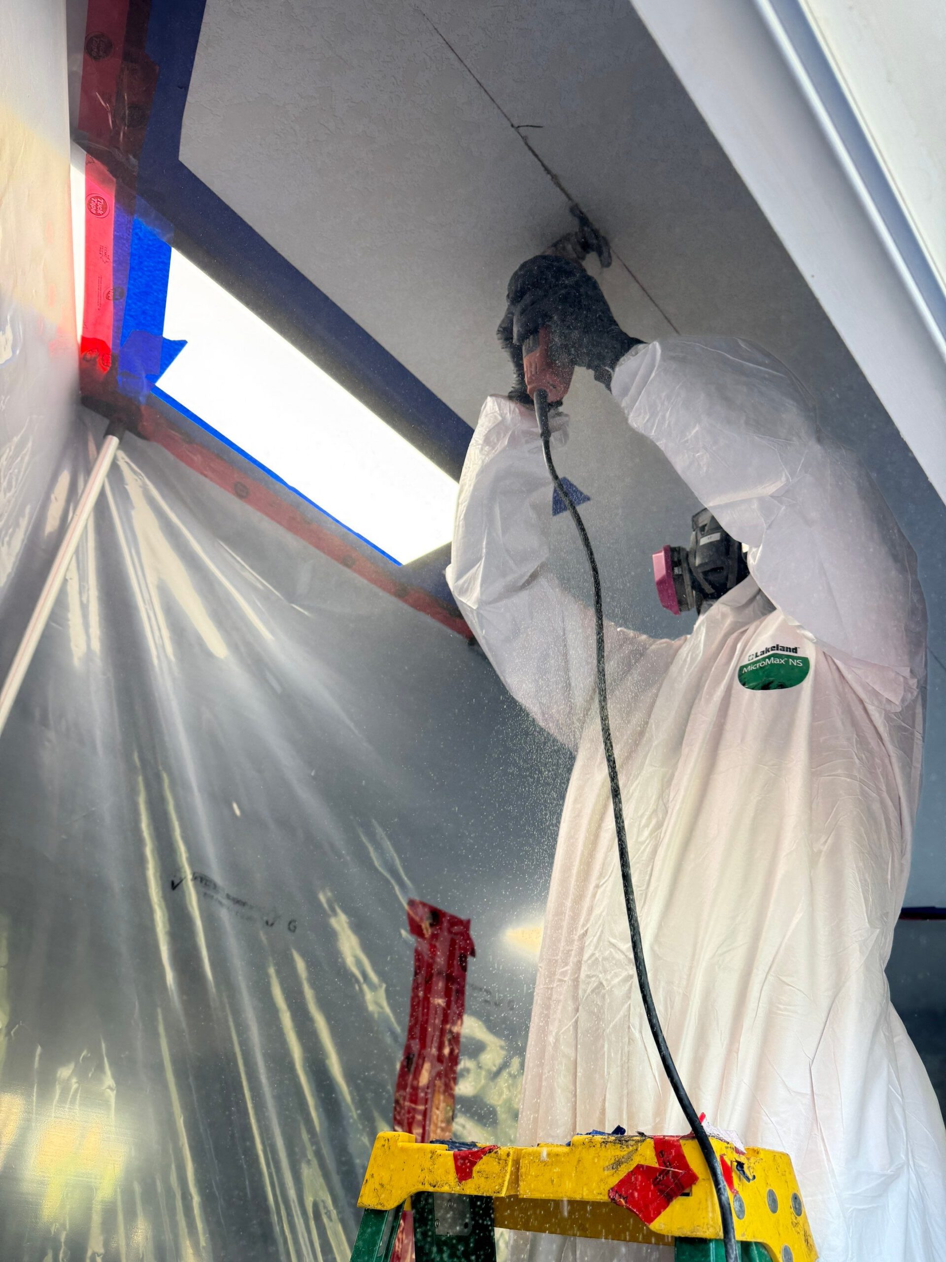 Worker in protective suit drilling into a ceiling inside a contained area