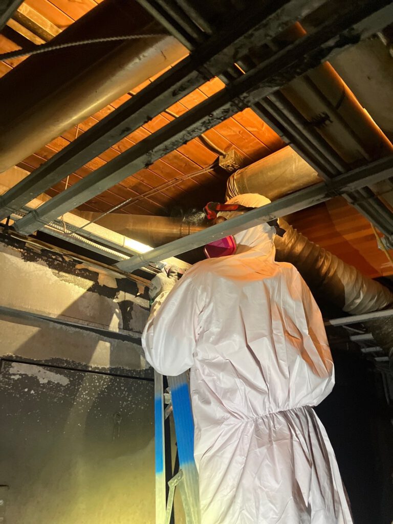Worker in protective suit on a ladder near exposed ceiling pipes