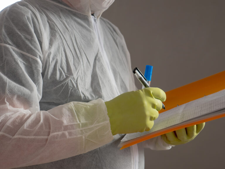 Gloved hands writing on a clipboard while wearing protective coveralls