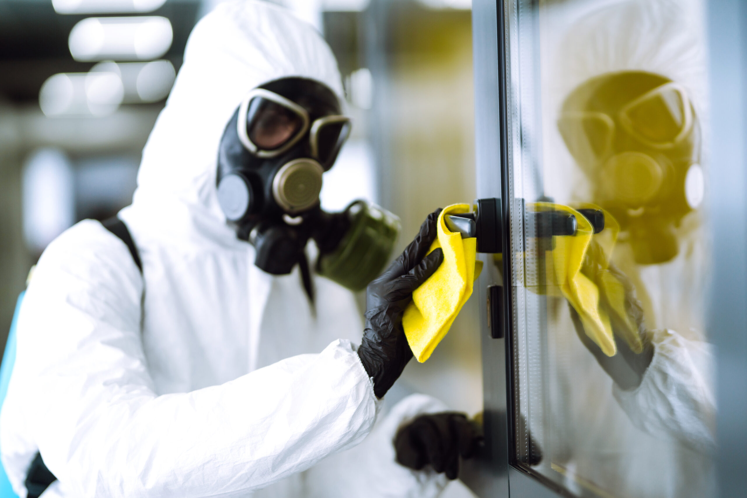 Worker in protective suit and respirator wiping a door handle