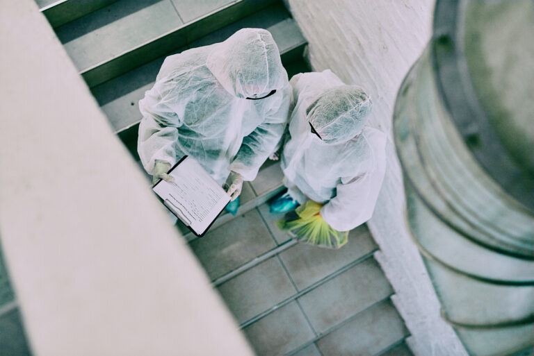 Two workers in protective suits standing on stairs with a clipboard